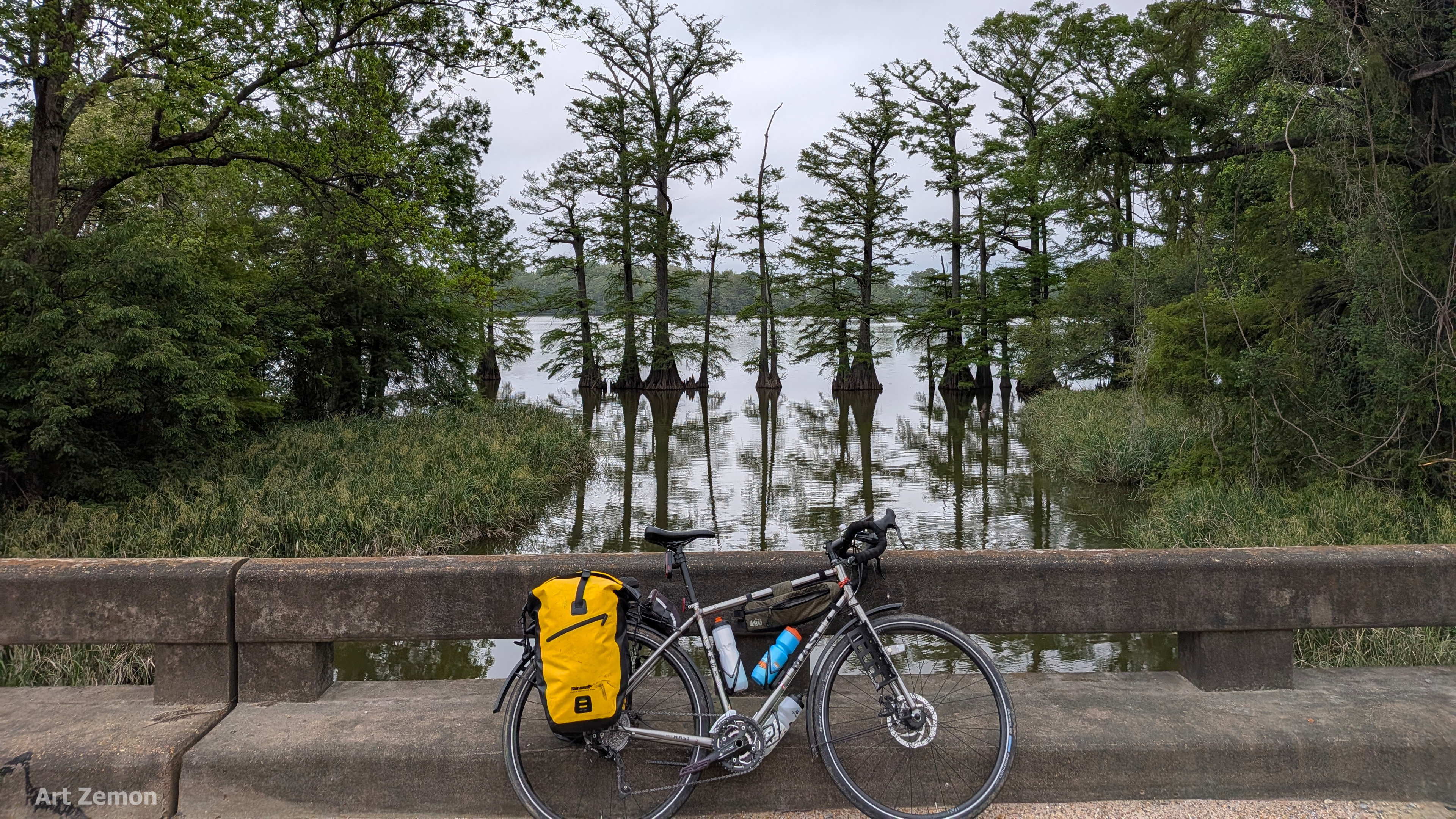 touring bicycle parked on a bridge. there is a lake in the background with cypress trees along the shallows