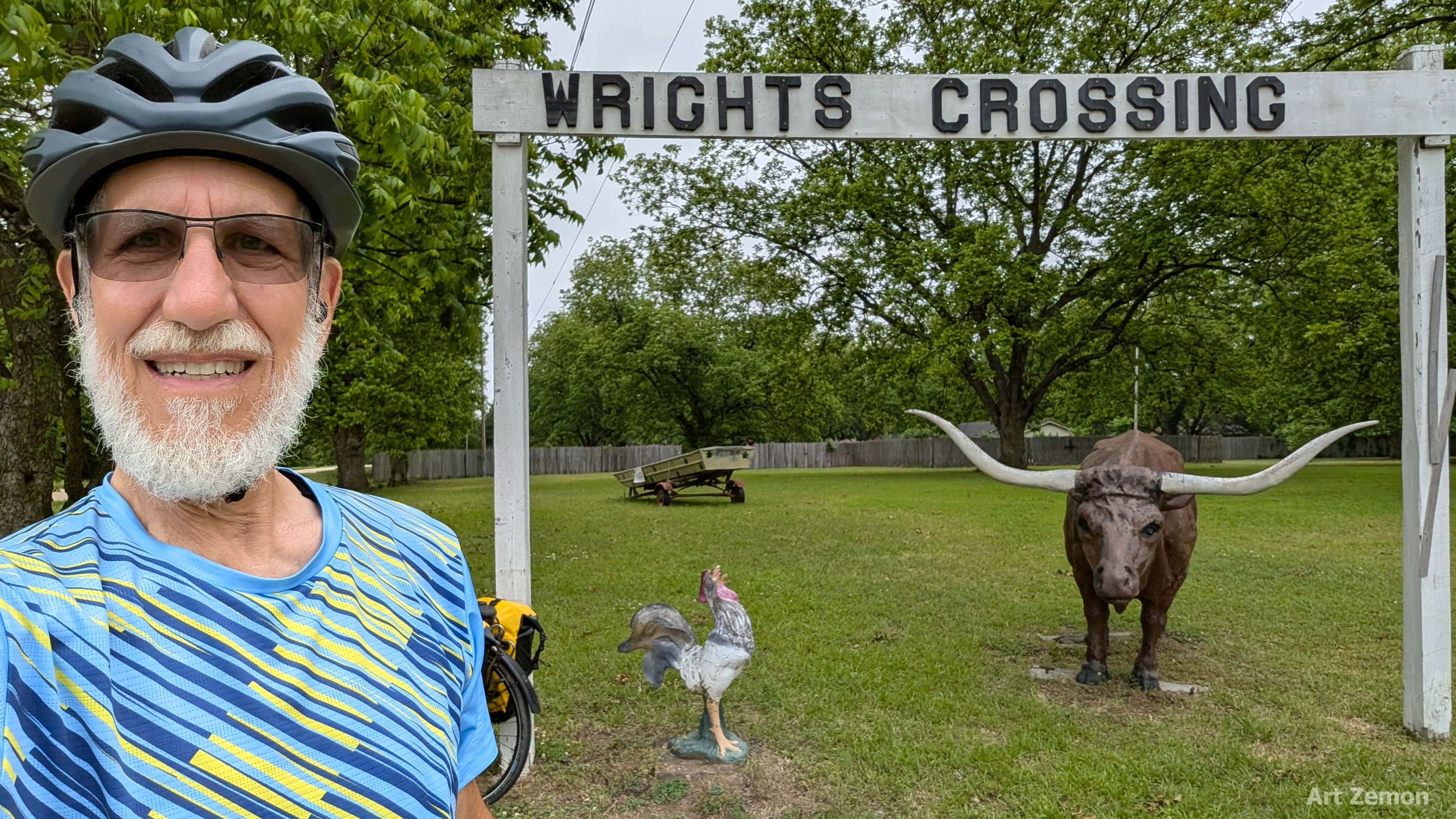 Art Zemon next to Writes Crossing arch with metal sculpted rooster and longhorn steer beneath