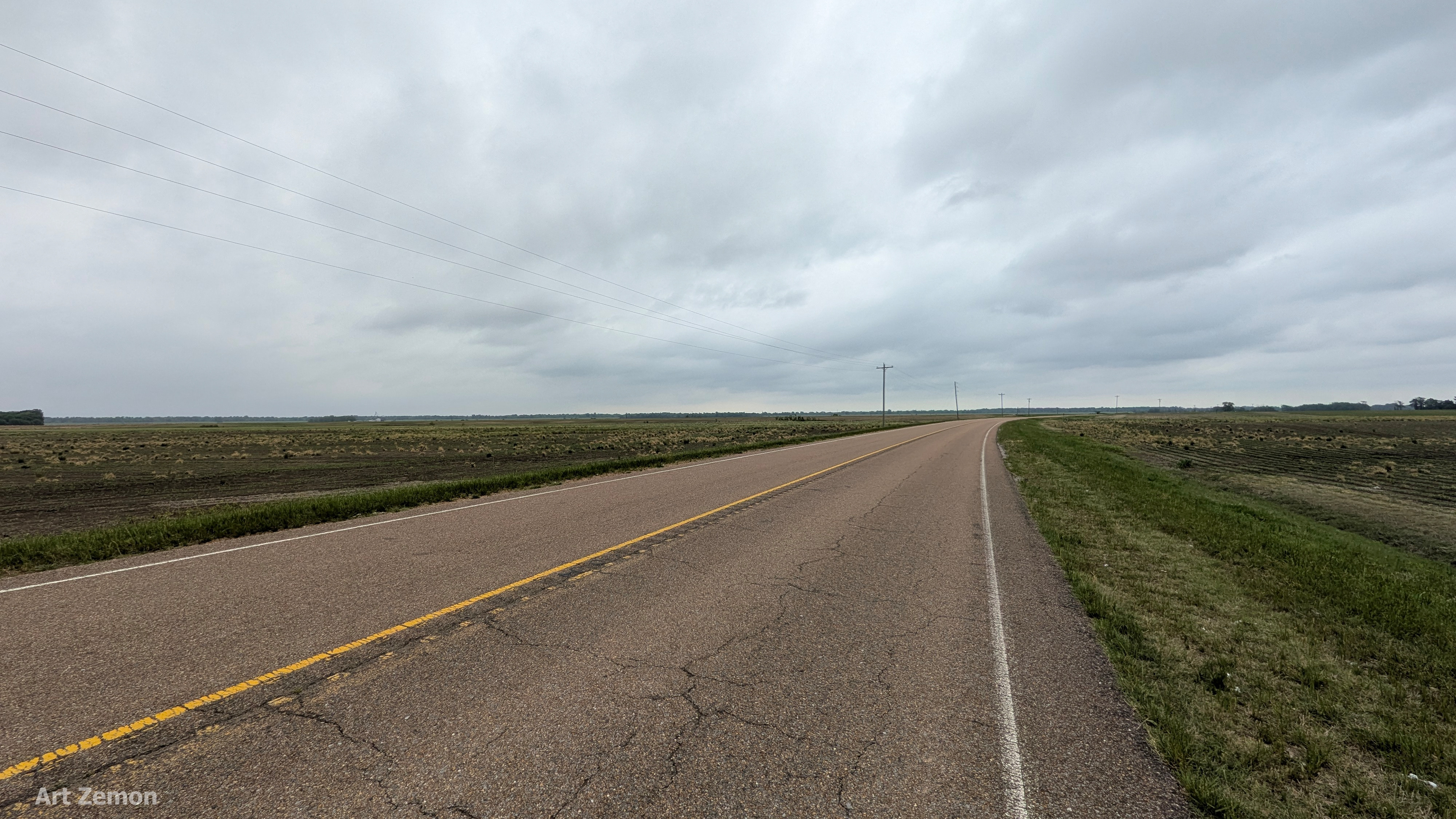 two lane road with empty fields on both sides and an overcast sky