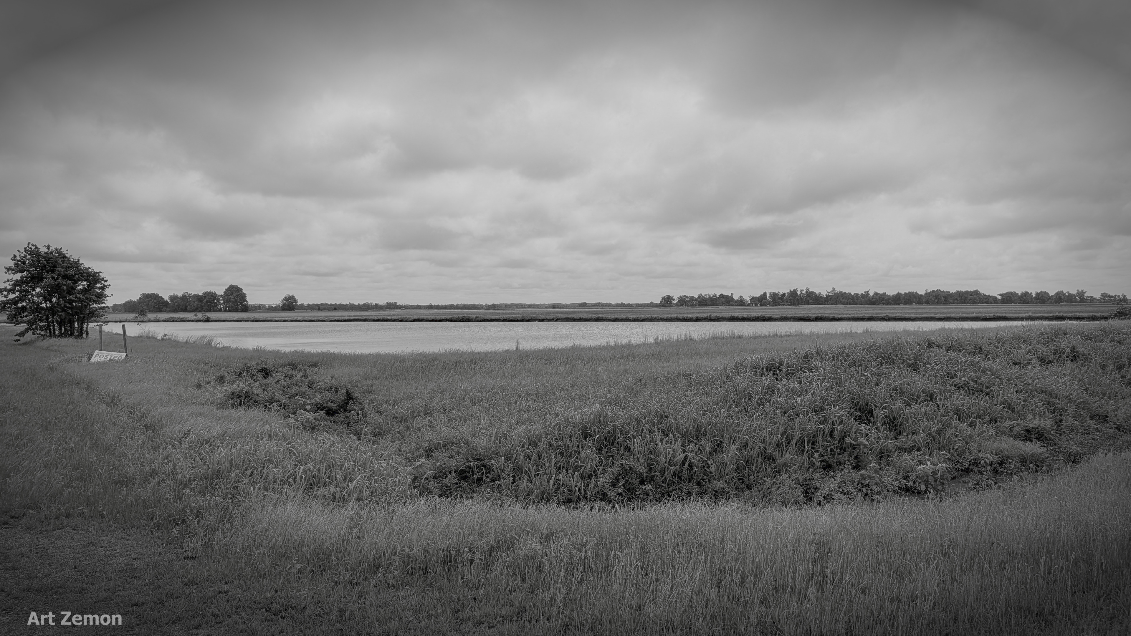 monochrome picture of a pond in a grassy field under overcast sky