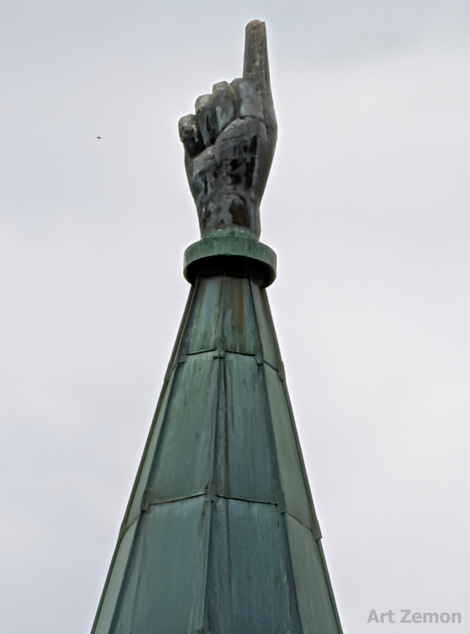 close-up of a church steeple. on top of the steeple is a large hand with the index finger pointing skyward