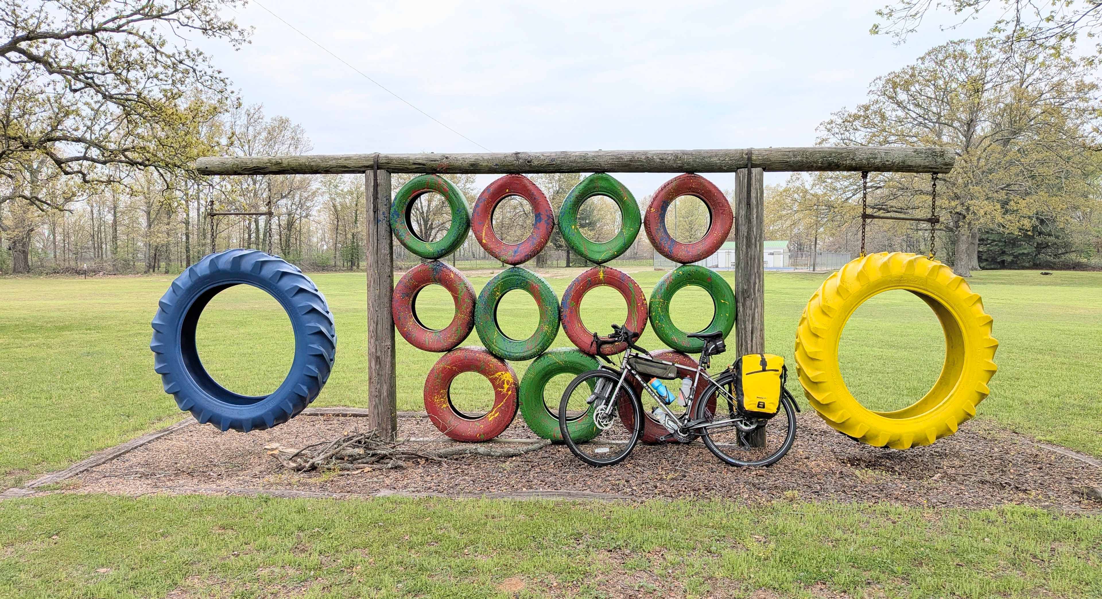 Touring bicycle parked in front of a playground climbing gym made from brightly painted tired