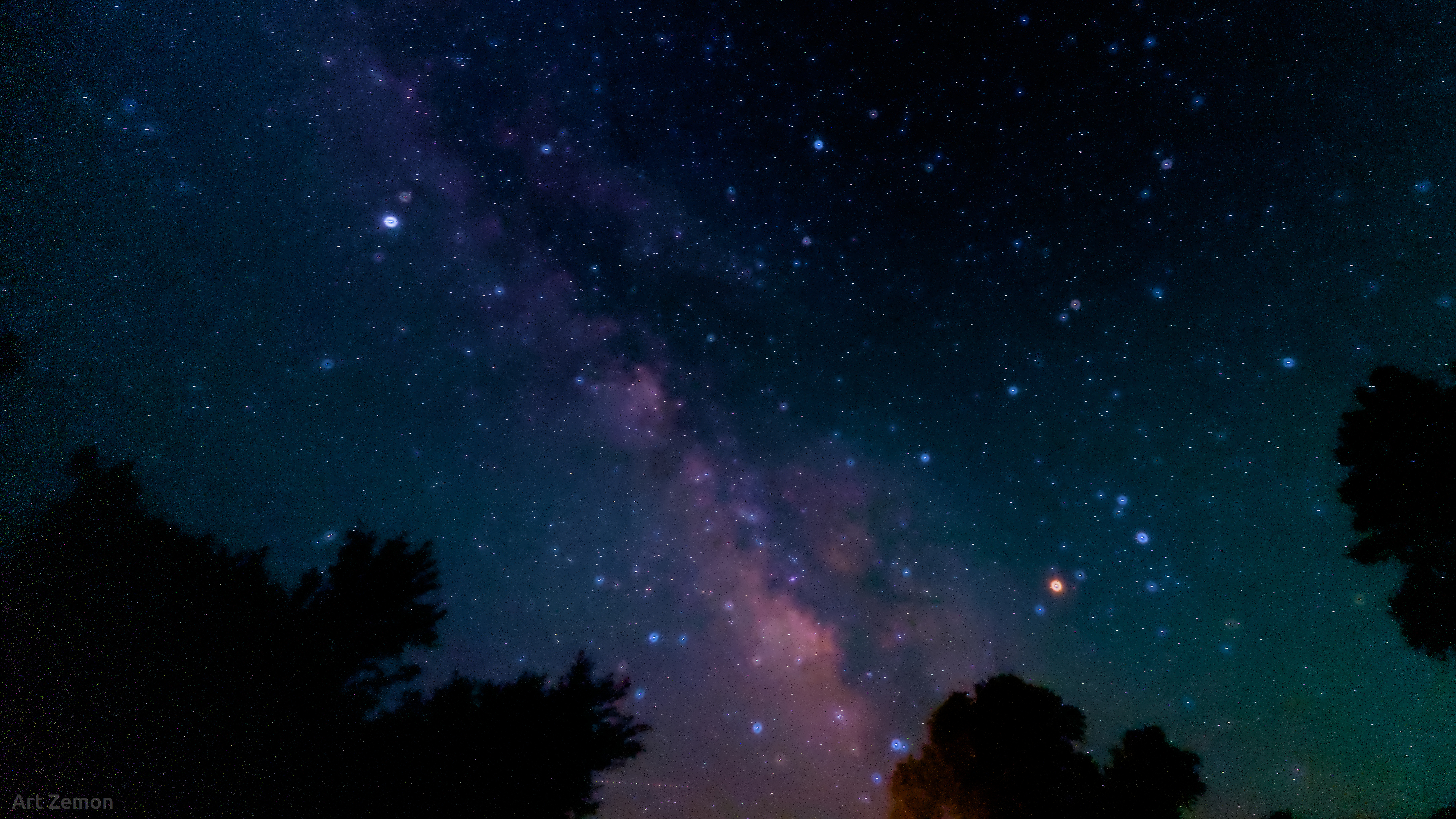 Night sky with Milky Way and many stars. The larger star have halos around them which are clearly different colors: white, yellow, orange, and blue.
